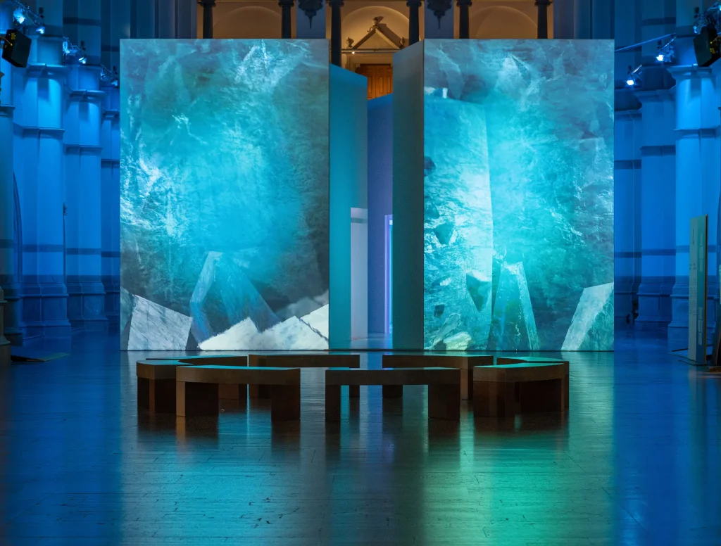 Ett uppbyggt isblock med videoprojektioner av smältande is i en stor utställningshall