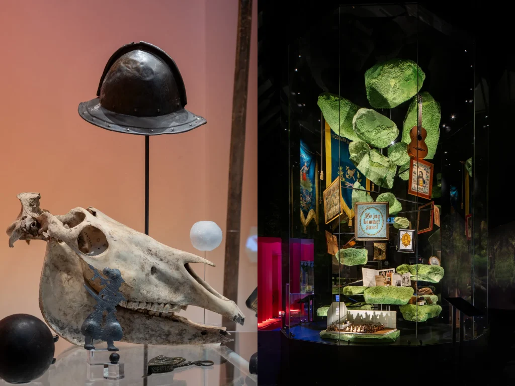 Två bilder i en: till vänster ett hästkranium och en soldathjälm på en glasskiva, till höger en cylinder med målningar, banderoller, gitarr och scenografi i form av mossbeklädda stenbumlingar.