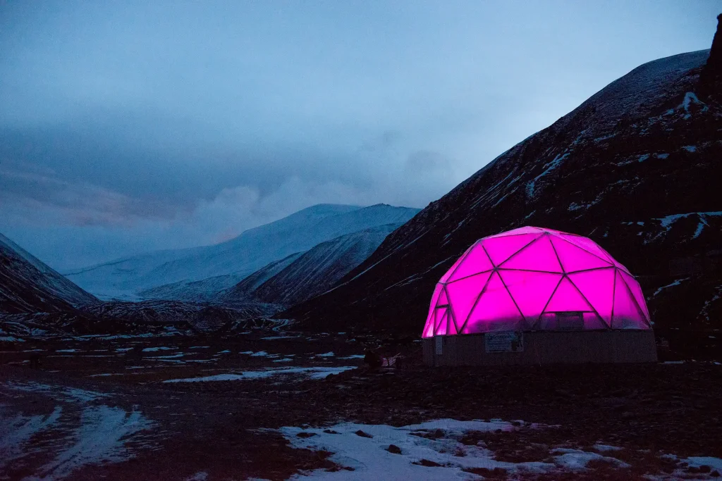 Ett kupoltält är uppslaget över en forskningsstation i Svalbards snöiga karga berg, ett starkt lila sken lyser i tältet.