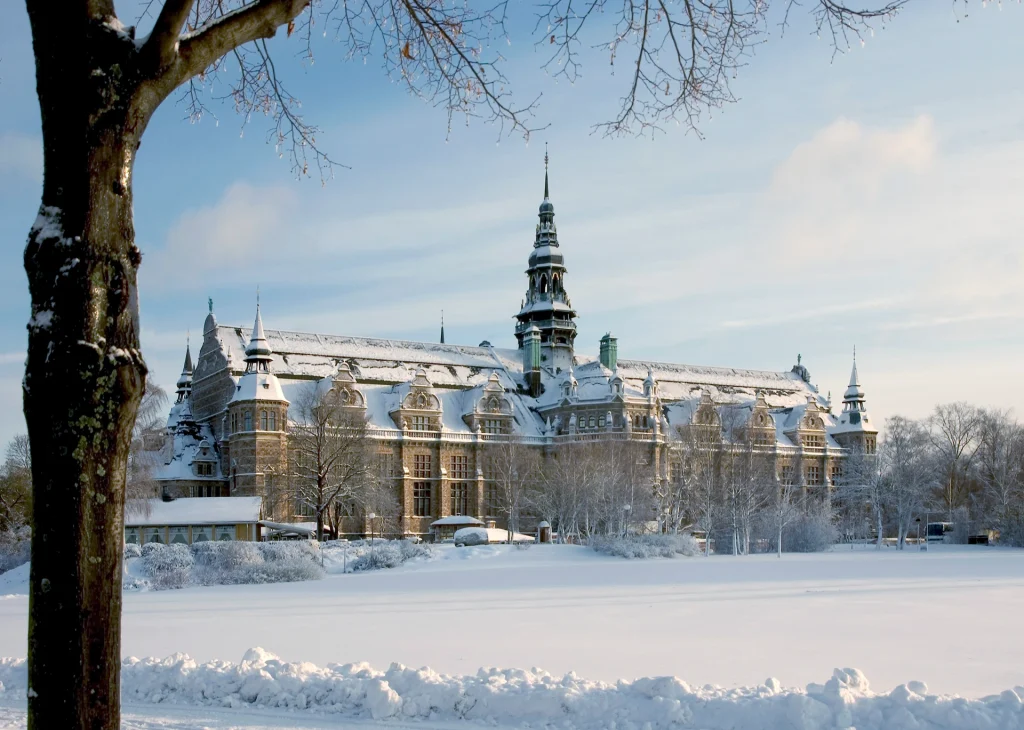 Nordiska museets baksida sett från Galärparken en klar vinterdag, djup snö ligger på marken och taket.