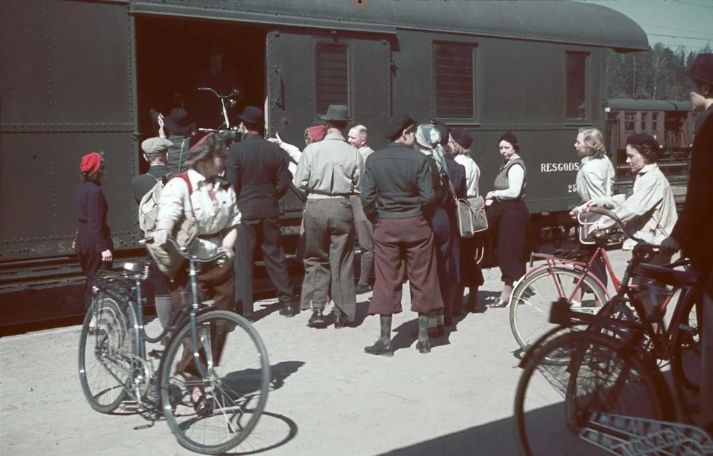 En tågvagn på en perrong med människor i 1930-talskläder som lastar på cyklar.