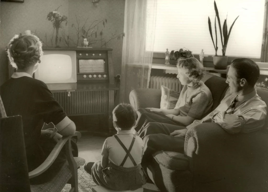 Två kvinnor, en man och en liten pojke sitter i ett vardagsrum vända från kameran mot sin nyköpta teveapparat.
